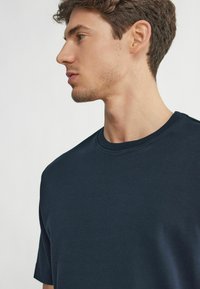 Marinblå t-shirt med kort ärm och rund halsringning, mjuk textur och minimala design detaljer. Tyget verkar slätt och flexibelt.