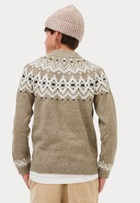 Maglione a maglia beige con un collo a pattina bianco e nero, polsini e orlo a costine, indossato sopra una camicia bianca. Il modello indossa un berretto beige chiaro.