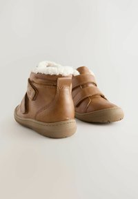 Braune Lederstiefeletten mit einem weichen weißen Fleece-Futter, ausgestattet mit verstellbaren Riemen, wasserdichtem Etikett und einer strukturierten Gummisohle.