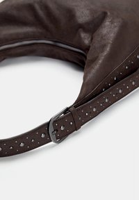 Braune Lederhandtasche mit weicher Textur, runder Form und einem strukturierten Tragegurt mit kreisförmigen Aussparungen und dunklem Hardware. Mit Reißverschluss.