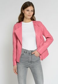 Lyserød læder bikerjakke med lynlås foran, lange ærmer og tætsiddende design. Bæres med en hvid t-shirt og grå jeans.