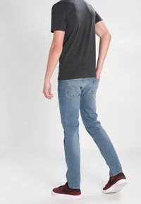 Ljusblå jeans i slim fit med bakfickor och subtila blekningar, kombinerade med en mörkgrå t-shirt och röda sneakers.