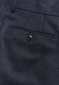 Tmavě modré kalhoty vyrobené z texturované látky, s jednou zadní kapsou na černý knoflík a diagonálním vzorem tkaní.