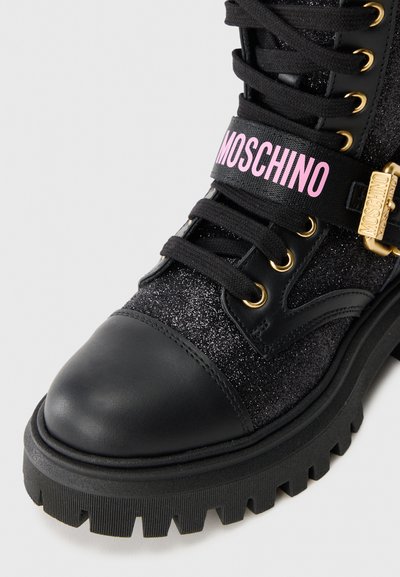 Sorte kampestøvlett med glitrende overdel, rund tå og en rosa stripe med "MOSCHINO" tekst. Gull detaljer er synlige.