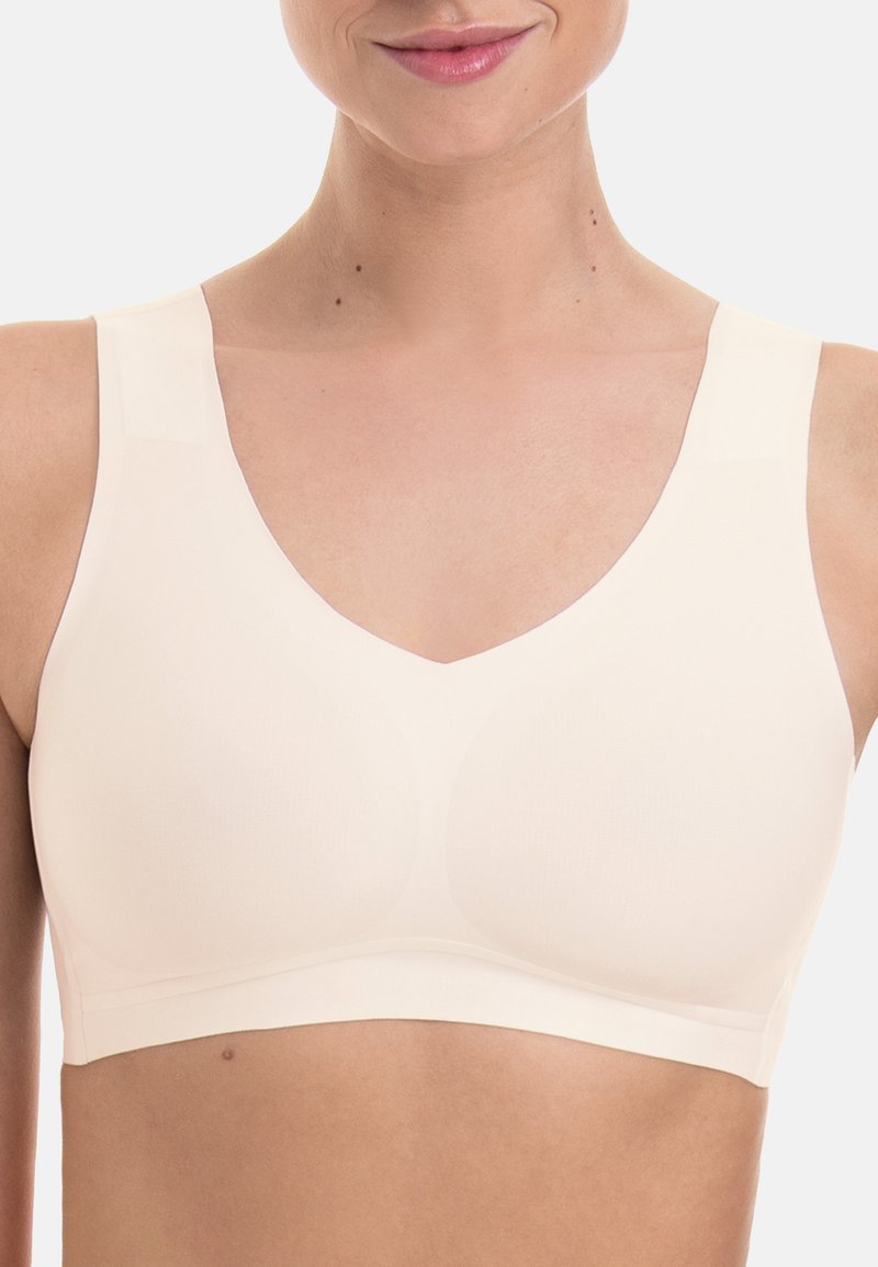 Light beige bralette with a v-neck design, wide straps, seamless finish, and smooth texture, featuring subtle contours for support.