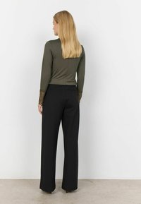 Top verde a maniche lunghe con dettagli in pizzo sulle maniche, abbinato a pantaloni neri a gamba larga. Abbigliamento mostrato dalla vista posteriore.