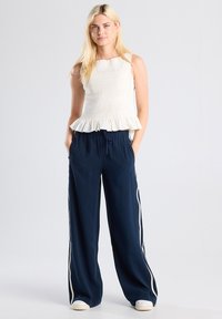 White smocked peplum top paired with navy wide-leg pants featuring white side stripes. Soft fabric, relaxed fit, minimalistic design.