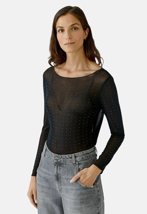 Schwarzer Langarm-Body aus transparentem Netzstoff mit gepunktetem Muster und Rundhalsausschnitt, kombiniert mit hellgrauen High-Waist-Jeans.
