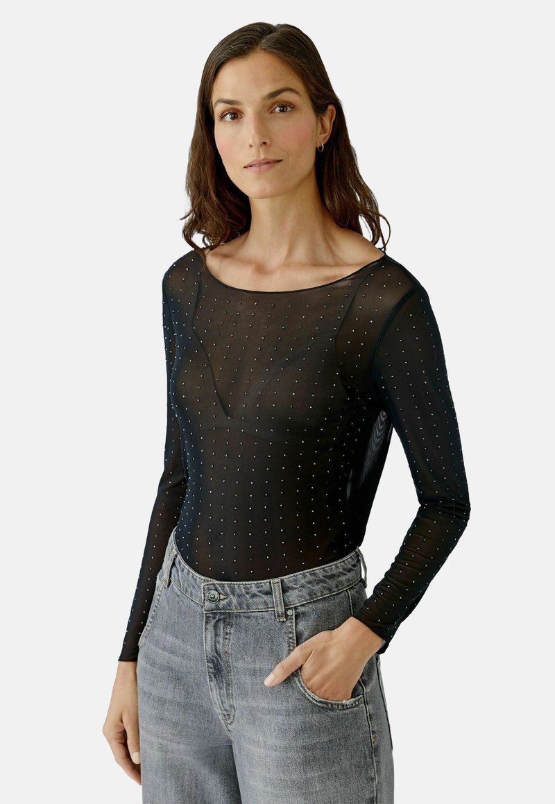 Schwarzer Langarm-Body aus transparentem Netzstoff mit gepunktetem Muster und Rundhalsausschnitt, kombiniert mit hellgrauen High-Waist-Jeans.