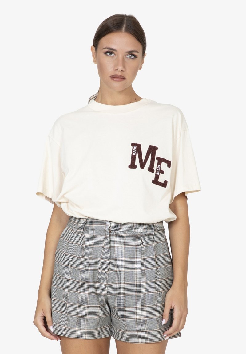 Cremfarbene Baumwoll-T-Shirt mit dunkelbraunen Nähten, auf denen "ME" steht, kombiniert mit hochtaillierten Karo-Shorts in Grau- und Beigetönen.