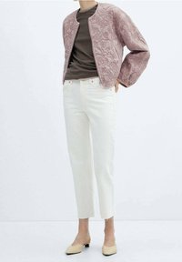 Giubbotto bomber trapuntato color rosa con colletto rotondo, abbinato a una maglietta marrone e jeans bianchi a vita alta. Accentuato da scarpe slip-on chiare.