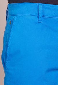 Blå bomullsblandning byxor med en jämn textur, slim fit-design, sidfickor och orange sömnadsdetalj nära midjan.