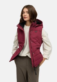 Bordowa pikowana kamizelka z kapturem, z przodu zamek błyskawiczny i zatrzaski, z czarną podszewką z polaru. Nosi się ją na kremowym swetrze.