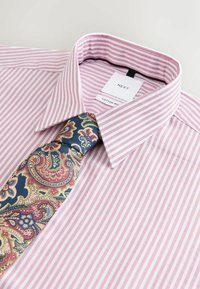 Chemise rayée en coton mélangé rose et blanc avec une cravate bleue à motifs paisley ornée d'accents rouges et verts, soigneusement disposée pour l'exposition.