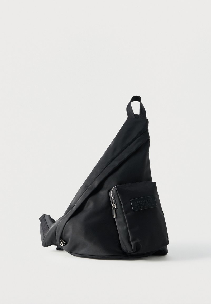 Black triangular crossbody bag with a front zip pocket and a top handle, set against a plain white background.