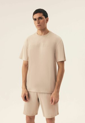Beige cotton t-shirt with short sleeves and embossed "HENDERSON" logo, paired with matching shorts, minimalistic design and soft texture.