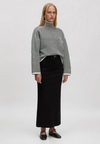 Gestreifter schwarz-weißer Rollkragenpullover mit herunterfallenden Schultern, kombiniert mit einem langen schwarzen Rock und schwarzen Ballerinas mit Bindebändern. Glatte Textilien.