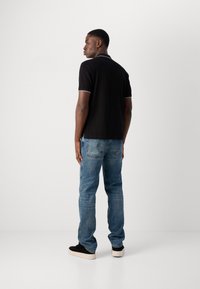 T-shirt polo noir avec col contrastant, assorti à un jean en denim bleu clair. Le modèle porte des chaussures noires avec une épaisse semelle crème.