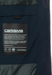 Navyblauer Stoff mit glänzender Oberfläche, ausgestattet mit einem rechteckigen schwarzen Etikett. Das Etikett enthält weißen Text, der die Markenwerte und Pflegeanweisungen umreißt.