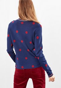 Maglione blu con pois rossi; scollo a costine con rifiniture bianche; texture morbida e design aderente; abbinato a pantaloni in velluto a coste rossi.