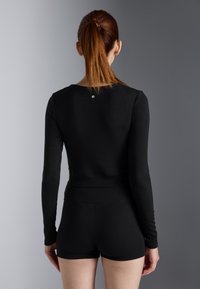 Crna long sleeve majica s prilagođenim dizajnom, rebrastom teksturom i malim logom straga. Uparena s odgovarajućim crnim šortsevima.