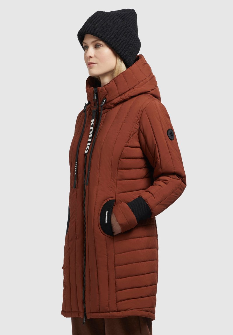 Braune gepolsterte Jacke mit Kapuze, gerippten schwarzen Bündchen, Reißverschluss und einem Logodetail. Verfügt über eine gesteppten Textur und seitliche Taschen.