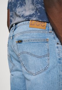 Jeans de mezclilla de un azul claro con una etiqueta de cuero de Lee en la cinturilla. Presenta costuras clásicas y dos bolsillos traseros con costuras curvadas.