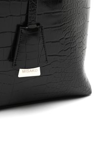 Črna torbica iz krokodilne usnjene teksture s strukturirano obliko, teksturirano površino in srebrno oznako z napisom "MISAKO", pritrjeno spredaj.