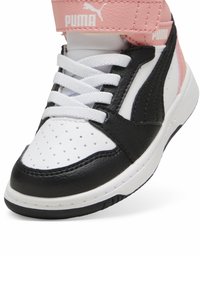 Baskets noir et blanc avec une sangle rose ; présente des perforations, une texture en cuir lisse et des lacets blancs. Logo Puma sur la sangle.