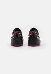 Chaussures de sport avec une tige noire texturée, rehaussée de détails jaunes et violets. Elles disposent d'un col rembourré et d'une semelle violette pour une meilleure adhérence.