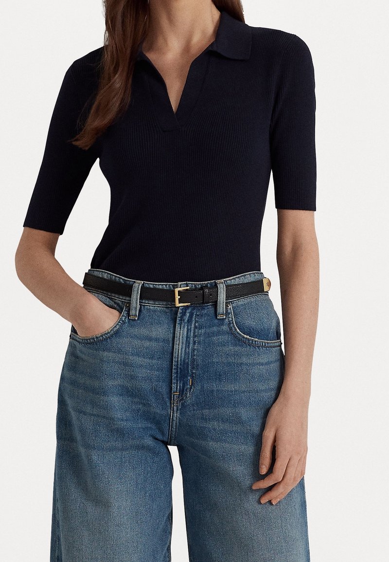 Polo shirt a coste blu navy con scollo a V, abbinato a jeans in denim blu a vita alta e una cintura in pelle nera con fibbia dorata.