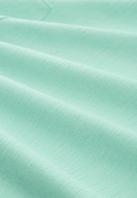 Jasno miętowa tkanina o gładkiej fakturze i subtelnym prążkowaniu, ukazana w fałdach, podkreślająca jej miękką, równą powierzchnię.