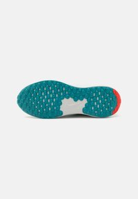 Suela de zapatilla blanca con una superficie de goma turquesa texturizada que presenta patrones hexagonales y un acento rojo en el talón.
