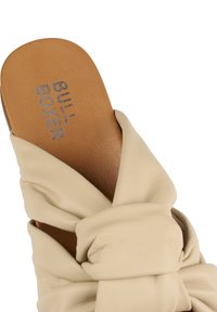 Béžové kožené skluzné sandály s uzlovým designem. Hnědá stélka s vyraženým logem "BULL BOXER". Hladká textura a minimalistický styl.