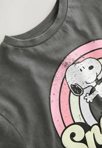 Grå T-shirt med rund hals i mjukt tyg, med en stor grafik av Snoopy mot en regnbågsbakgrund i rosa, gult och grönt.