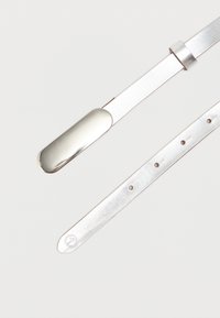 Valkoisesta tekonahasta valmistettu hihna, jossa on sileä pinta, metallinen yksityiskohta ja useita säätöreikiä koon mukauttamiseen.