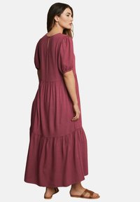 Bordeaux maxi Kleid mit Puffärmeln, gestuftem Design, Schlüsselloch-Rücken und weicher Textur. Kombiniert mit braunen Sandalen für einen vollständigen Look.