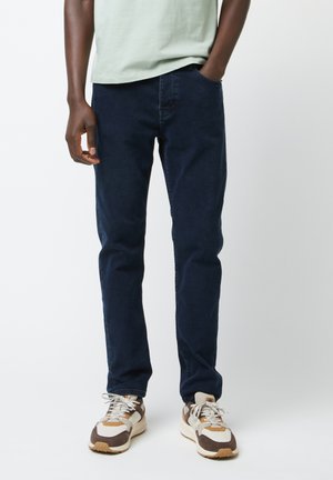 Jeans blu navy con vestibilità slim, realizzati in denim, dotati di tasche frontali e una texture sottile. Abbinati a sneakers multicolori.