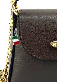 Bruine leren handtas met gestructureerde afwerking, gouden kettingband en een zilveren bedel met de Italiaanse vlag. Ontwerp met gesloten klep.