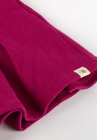 Fuchsia Pullover mit einer weichen Textur, ausgestattet mit einem umgeschlagenen Saum und einem kleinen, gebrandeten Etikett mit einem goldenen Design, das am Rand angebracht ist.