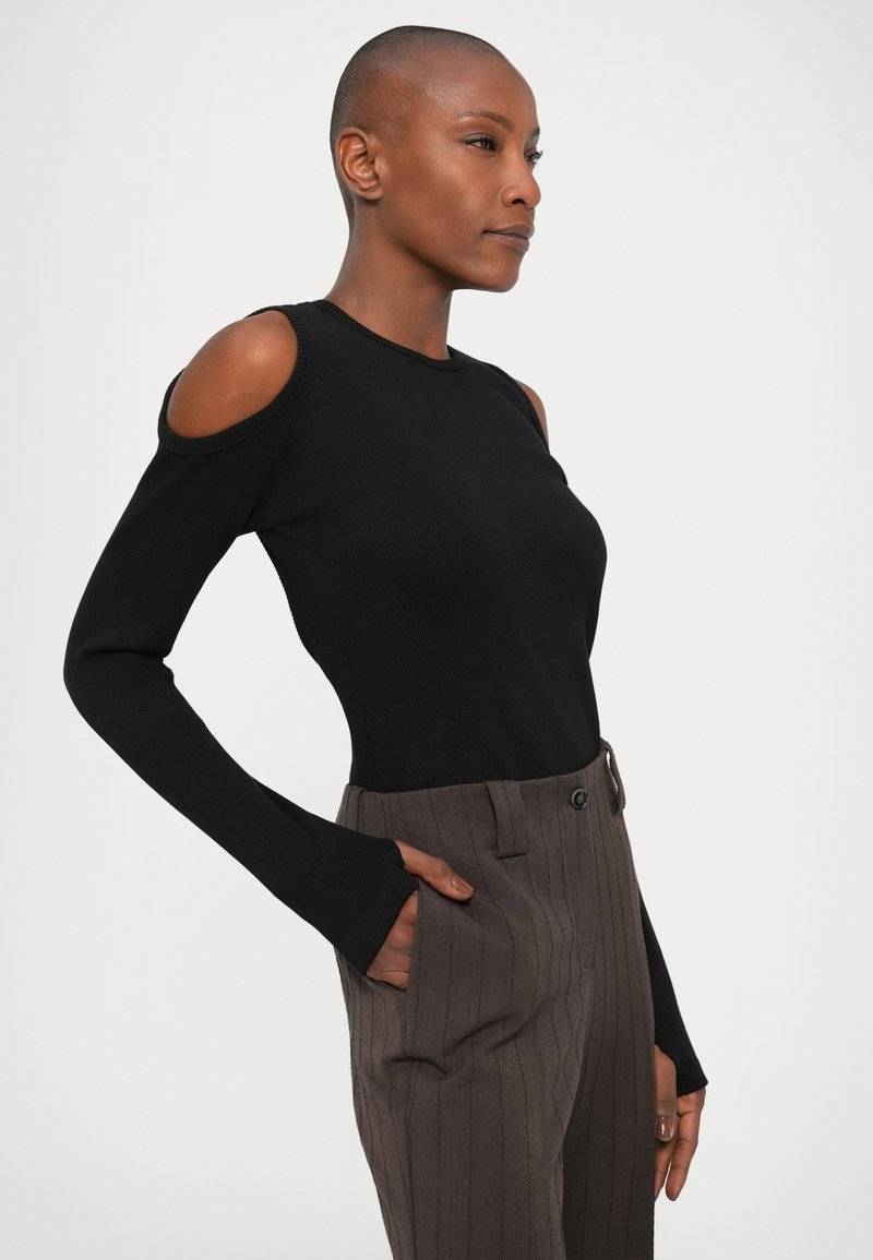 Haut noir à manches longues avec des épaules dénudées, texture côtelée et silhouette ajustée. Associé à un pantalon taille haute à rayures fines marron.