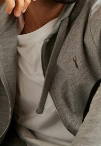 Gray zip-up hoodie with a textured finish and a small embroidered lobster logo. Worn over a white round-neck T-shirt.