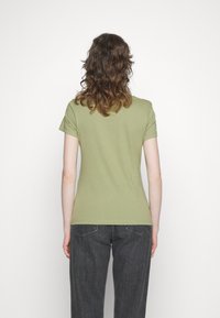 T-shirt en coton vert olive à manches courtes, au design ajusté et au col rond. Porté avec un jean gris foncé, vu de dos.