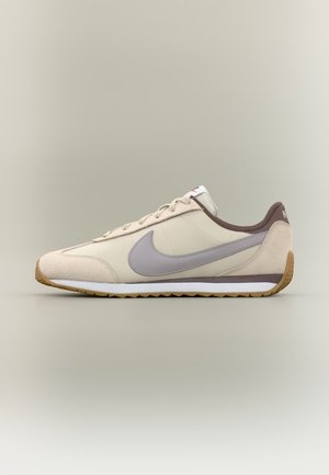Baskets Nike beige et marron clair avec logo swoosh gris, fermeture à lacets et semelle blanche avec semelle extérieure en gomme, vue de côté sur fond neutre.