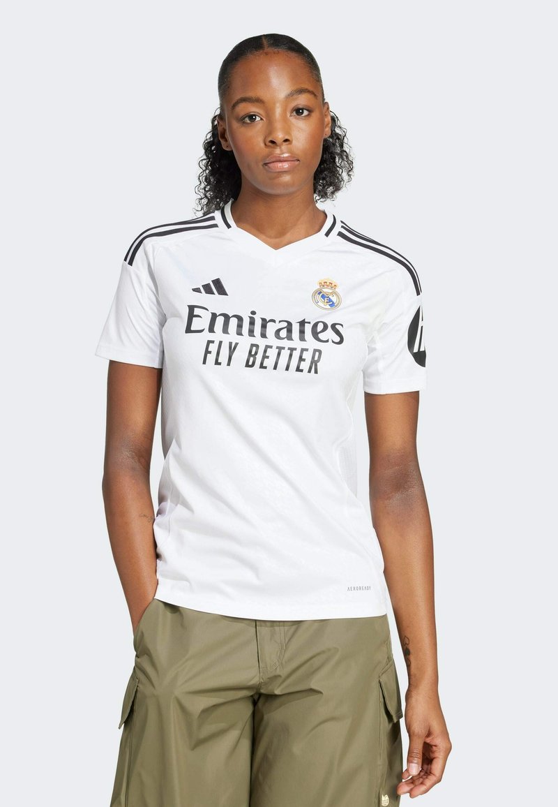 White Adidas jersey with black stripes, "Emirates Fly Better" logo, club crest, and v-neck design. Worn with olive green cargo pants.