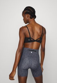 Sutiã desportivo preto com alças cruzadas nas costas, combinado com calções cinzentos com padrão, apresentando um bolso na cintura e um design texturizado.