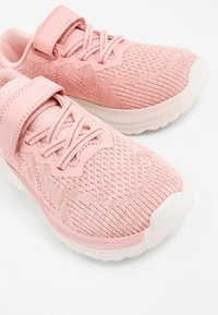 Rosa Sportschuhe mit einem strukturierten Strick-Obermaterial, verstellbarem Riemen und weißer Sohle mit einer leichten Biegung an der Zehe.