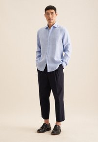 Lichtblauwe linnen overhemd met een button-down kraag, lange mouwen, voorflap, gecombineerd met donkere broek en zwarte schoenen.
