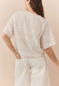 Maglione morbido di colore chiaro, con una vestibilità ampia e corta, abbinato a pantaloni a vita alta color crema con tasche laterali.