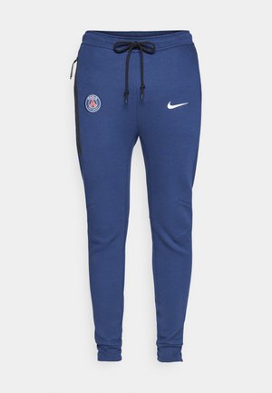 Siniset urheiluhousut, joissa on nyöri vyötäröllä, sivutaskut vetoketjulla, mustat yksityiskohdat ja logot: PSG:n emblem ja Nike-logomerkki.